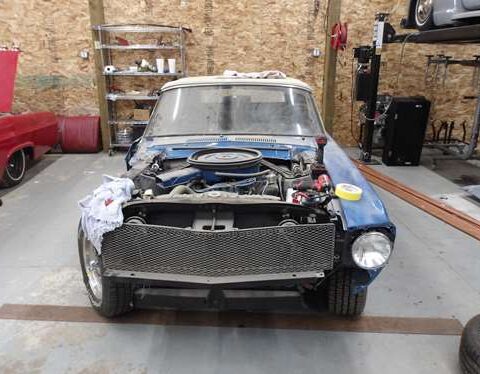 Classic car mid-restoration with exposed engine and removed front panels.