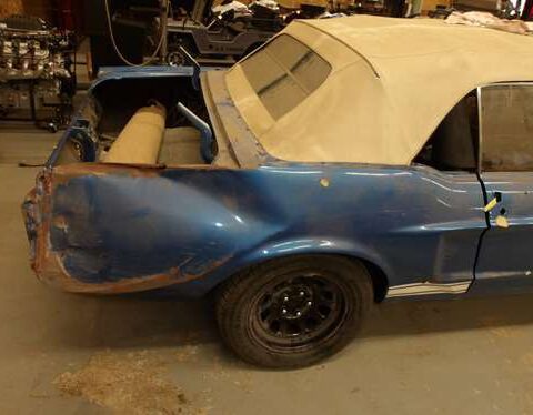 Blue convertible car with a damaged rear side in a garage.