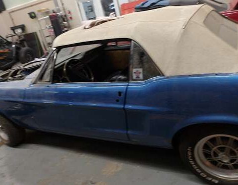 Vintage blue convertible car with a beige soft top in a garage.