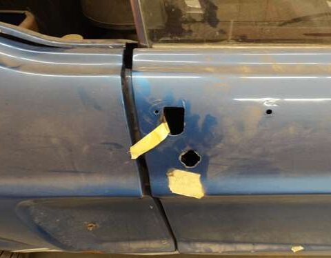 Car door with missing handle and taped areas on a blue vehicle.