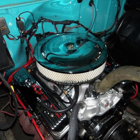 Close-up of a classic car engine with a round air filter and blue body.