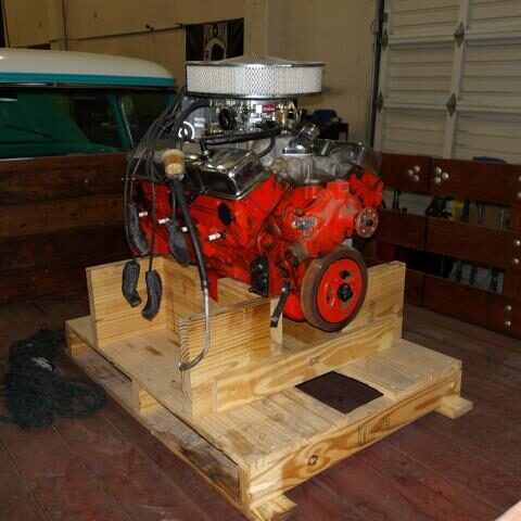 A bright red car engine mounted on a wooden pallet in a garage.
