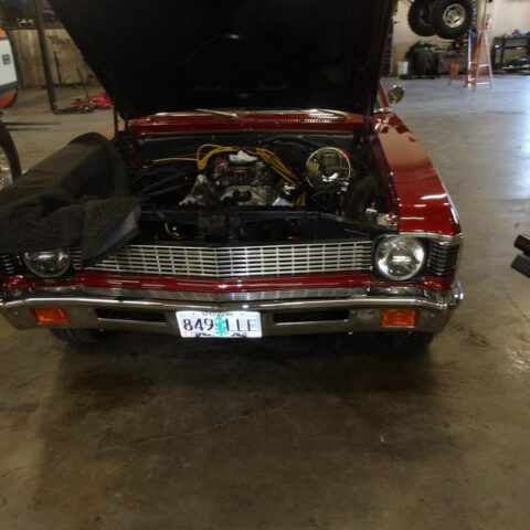A classic red car with its hood open in a garage.