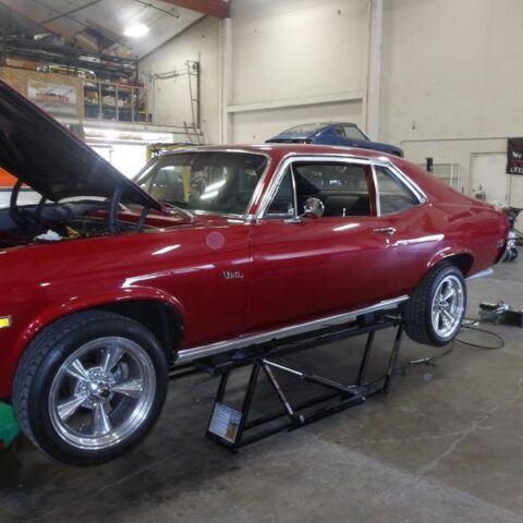 Classic red muscle car in a garage with hood open.