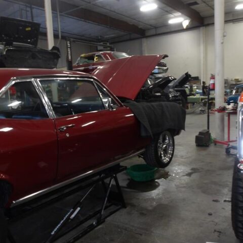 Red car being repaired in a garage with its hood open.