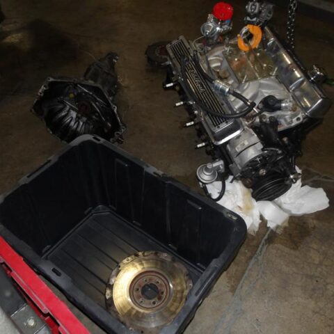 Disassembled engine parts placed on a workshop floor with a container collecting fluid.