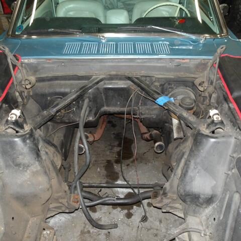 Empty car engine bay with wiring and hoses visible.