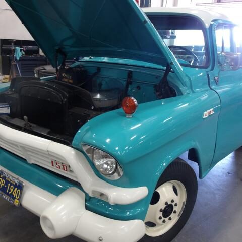 A vintage turquoise truck with its hood open in a garage.