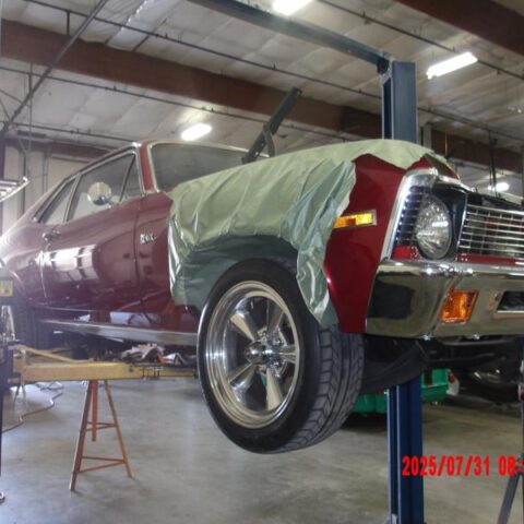 A classic red car on a lift undergoing restoration in a garage.
