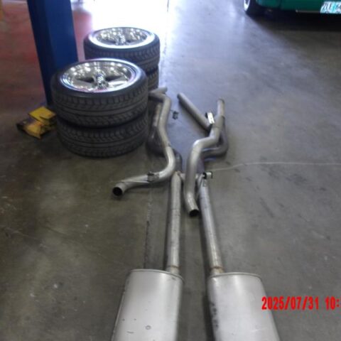 Two car exhaust mufflers with pipes on the floor near stacked tires.