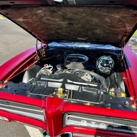 Open hood of a red classic Pontiac car showing engine.