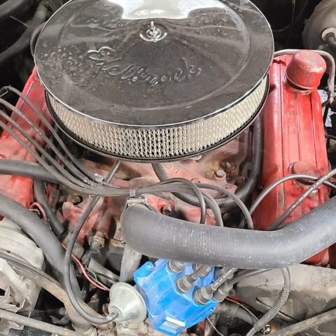 Close-up of a classic car engine with a round air filter and red valve covers.