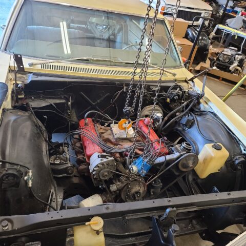 Car engine bay with a partially disassembled engine in a workshop.