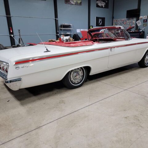 Classic white convertible car with red interior in a garage.