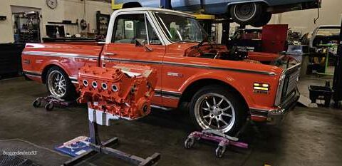 Classic orange pickup truck undergoing engine restoration in a garage.