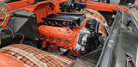 An orange engine installed in a classic car with plaid upholstery.