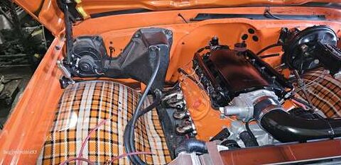 Partially restored classic car engine bay with plaid seat upholstery.