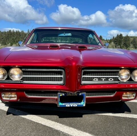 Front view of a classic red Pontiac GTO under a blue sky.