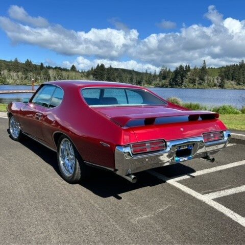 Classic red muscle car parked near a lake on a sunny day.