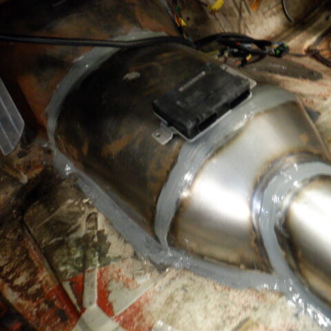 Close-up of a metal catalytic converter under a vehicle.