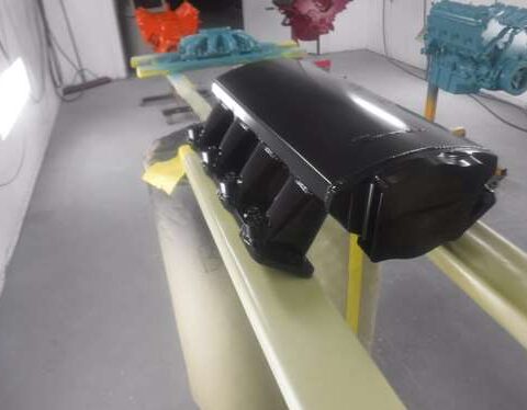 Black intake manifold placed on a yellow support in a workshop.