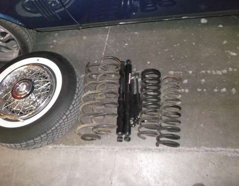 Various metal springs and shock absorbers laid out on the ground near a tire.